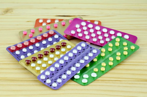 Pílula contraceptiva oral colorida tiras na mesa de madeira de pinho . — Fotografia de Stock