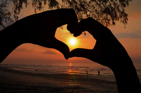 Salida del sol en el marco del corazón de la mano en vista a la playa . — Foto de Stock