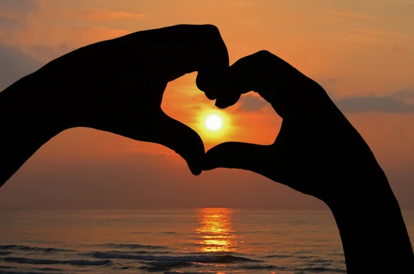 Salida del sol en el marco del corazón de la mano en vista a la playa . — Foto de Stock
