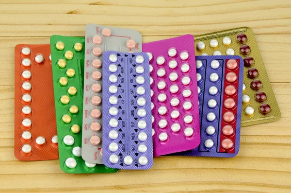 Colorful oral contraceptive pill strips on pine wood table. — Stock Photo, Image