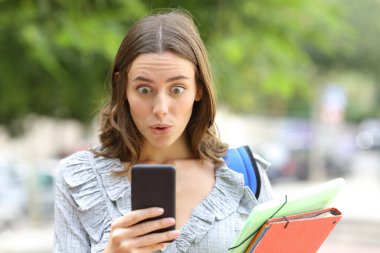 Sokakta cep telefonunu kontrol eden şaşırmış bir öğrencinin portresi.