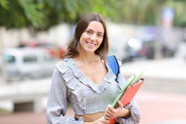 Caddede duran dosyalarla kameraya bakan mutlu öğrenci.