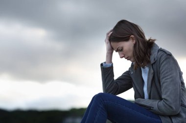 Bulutlu bir günde yalnız oturan üzgün bir kadının profili