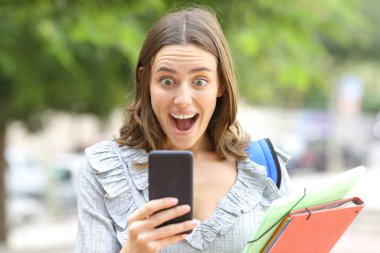 Şaşırmış bir öğrencinin sokakta yürürken akıllı telefon haberlerini kontrol etmesi.