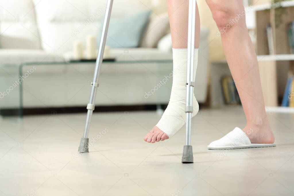 Side view portrait of a disabled woman with bandaged foot walking with crutches at home