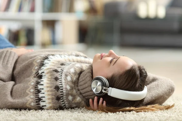 Relaxed teen listening to music wearing headphones lying at home in winter