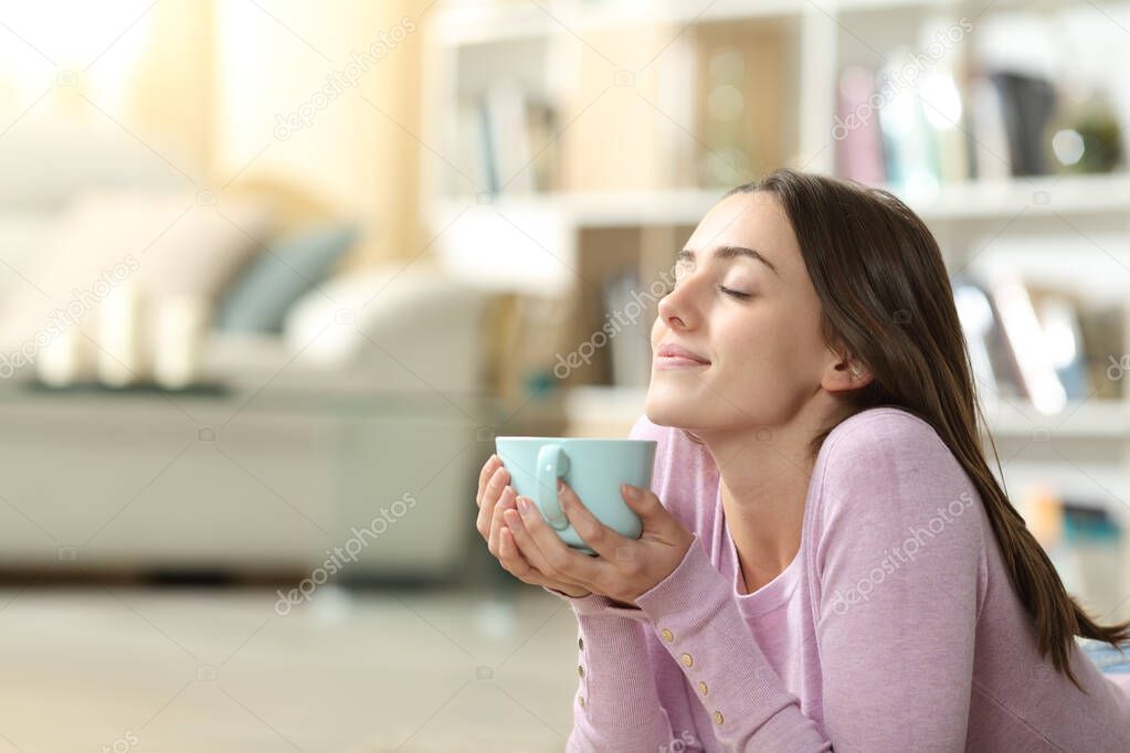 Relaxed woman enjoying of a coffee cup smelling lying at home