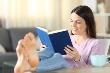 Evdeki oturma odasında kitap okuyan mutlu kadın.