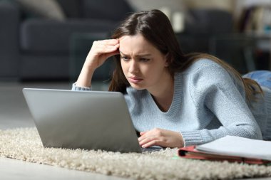 Evde yerde yatan dizüstü bilgisayarla kafası karışmış bir öğrenci e-öğreniyor.