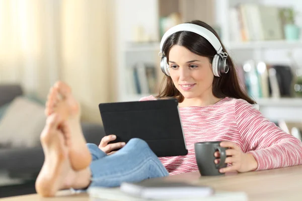 stock image Happy woman watching video with tablet and headphones sitting at home