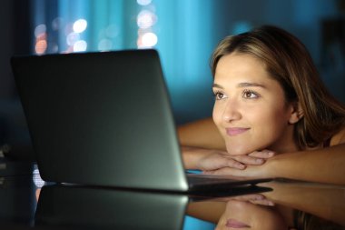 Gece evde dizüstü bilgisayardan medya içeriğini izleyen tatmin olmuş bir kadın.