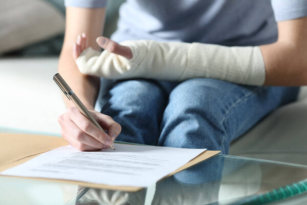 Close up portrait of a disabled woman with bandaged arm sigining insurance document