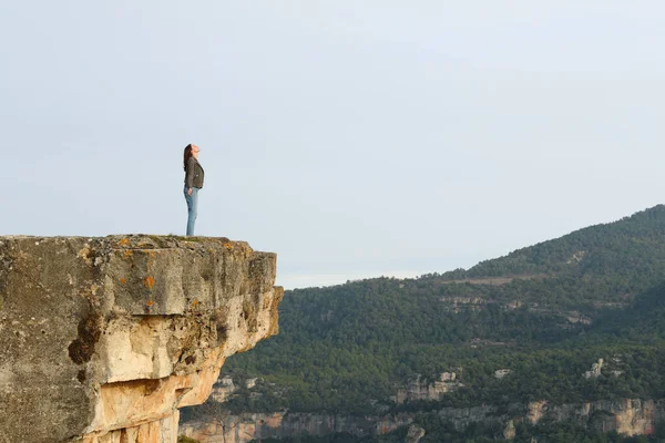 Full body portrait of a woman breathing fresh air in the top of a cliff in the mountain