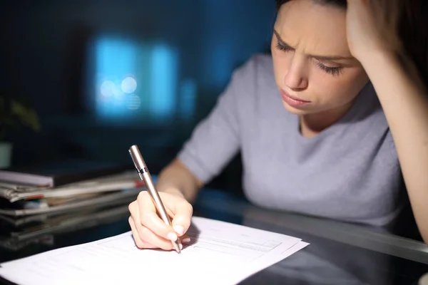 Worried woman filling paper form in the night at home