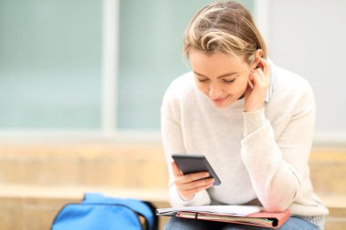 Öğrenci akıllı telefonu kontrol ediyor. Merdivenlerde oturuyor.