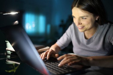 Evdeki oturma odasında dizüstü bilgisayar kullanan mutlu bir kadın.