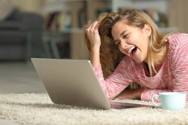 Komik kadın yüksek sesle gülüyor dizüstü bilgisayarla evde yerde yatıyordu.