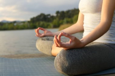 Gün batımında bir gölde yoga yapan kadın elleri.