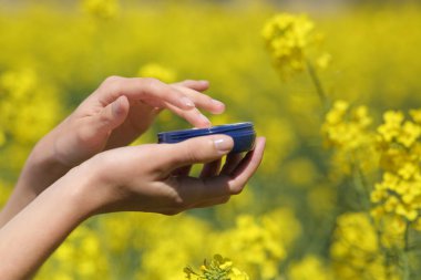 Bahar mevsiminde sarı bir tarlada elinde nemlendirici kavanozu tutan bir kadının fotoğrafını çek.