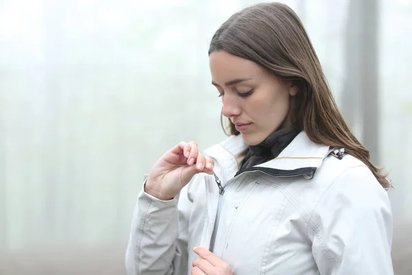 Hiker woman zipping the jacket ready to walk in a foggy forest