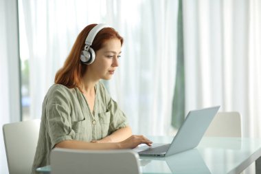 Concentrated woman with wireless headphones checking laptop at home