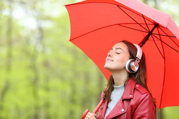 Relaxed Woman Red Holding Umbrella Rain Listening Music Wearing Wireless — Stockfoto