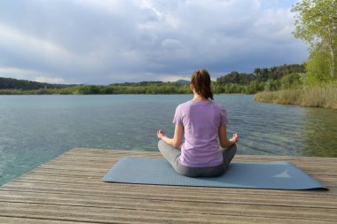 Güzel, sakin bir göl iskelesinde yoga yapan bir kadının arka plan portresi.