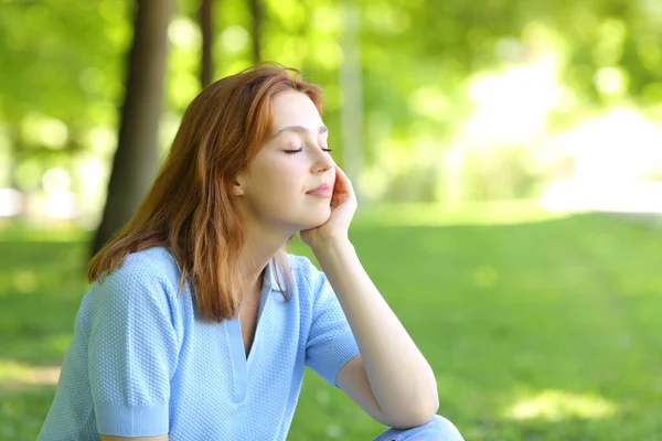 目を閉じて公園に座っているリラックスした赤毛の女性 — ストック写真