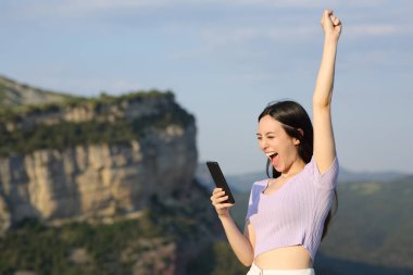 Heyecanlı Asyalı kadın tatilde dağda akıllı telefonu kontrol ediyor.