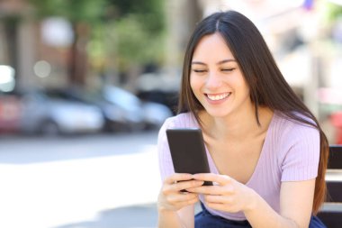 Sokakta bankta oturan akıllı telefon kullanan Asyalı kadın.