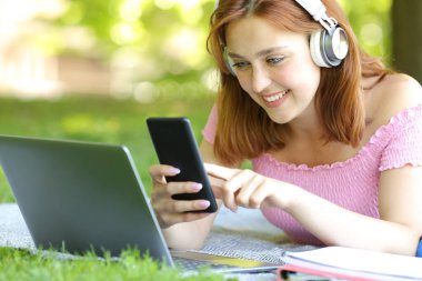 Parkta bilgisayar ve akıllı telefon kullanan kulaklık takan mutlu bir öğrenci.