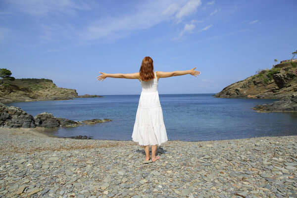 Back view full body portrait of a woman in white dress stretching arms on the beach
