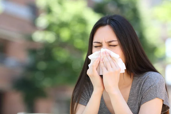 Ill asian woman blowing on tissue outdoors in the street