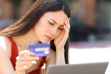 Sokakta kredi kartı ve laptopla internetten almakta zorlanan endişeli bir kadın.