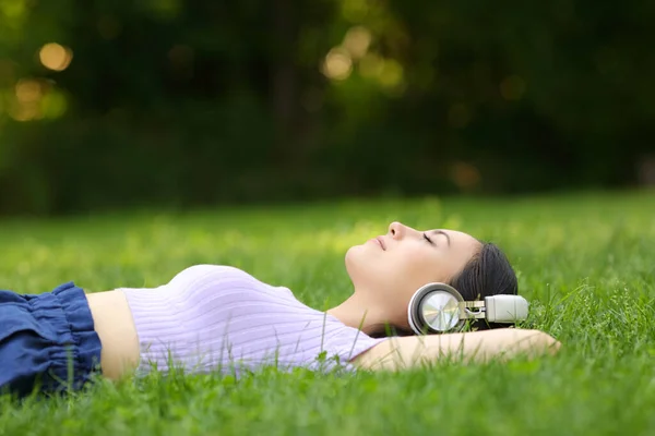 公園で草の上でリラックスしてヘッドフォンを身に着けている音楽を聞いているアジアの女性のプロフィール — ストック写真