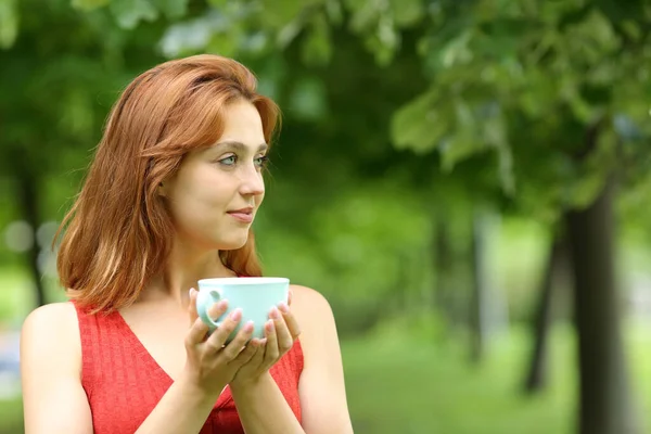 一个严肃的女人拿着咖啡杯 凝视着公园里的风景 — 图库照片