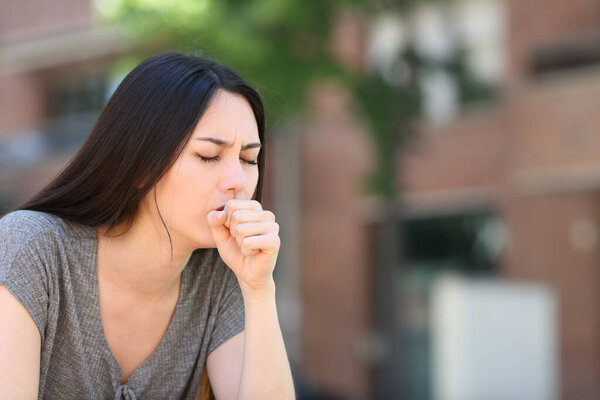 Ill asian woman coughing covering mouth with her hand in the street
