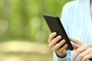 Ormanda yürürken akıllı telefon kullanan bir kadının ellerini kapat.