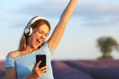 Müzik dinleyen, kulaklık takan ve lavanta tarlasında şarkı söyleyen mutlu kadın