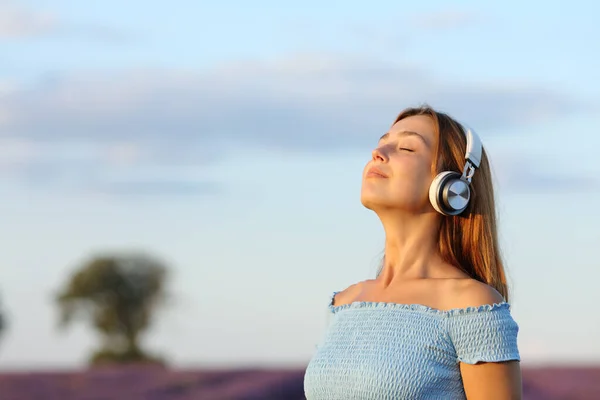 ラベンダー畑でワイヤレスヘッドフォンで音楽を聞いて呼吸する幸せな女性 — ストック写真