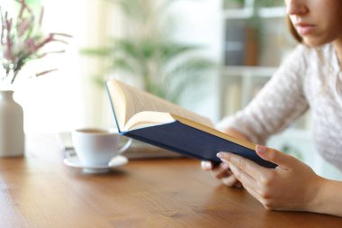 Evde kitap okuyan bir kadının ellerinin yakın portresi.