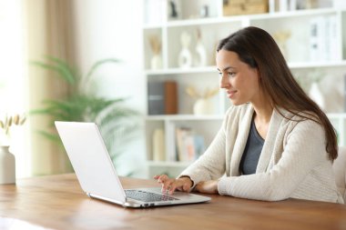Evin içindeki ahşap bir masada dizüstü bilgisayarda gezinen bir kadın.