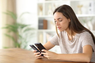 İki akıllı telefonu kontrol eden kadın eve yenisini yerleştiriyor.