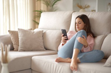 Evdeki koltukta cep telefonunu kontrol eden ciddi bir kadın.