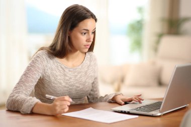 Ciddi bir kadın evdeki bilgisayardan internet bilgilerini kontrol ediyor.