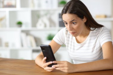 Kafası karışmış bir kadın evin içinde cep telefonundan saçma içerikleri kontrol ediyor.