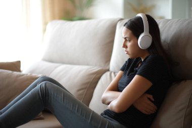 Üzgün kadın evde tek başına bir kulaklıktan gelen sesi dinlemekten şikayetçi.