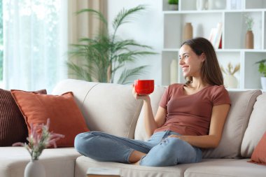 Teras renginde mutlu bir kadın. Kahve içiyor. Evdeki bir kanepede oturuyor.