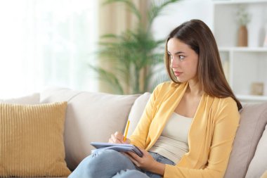 Sarı çizen ve başka tarafa bakan kadın evdeki kanepede oturuyor.