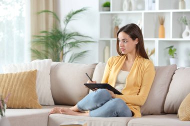 Dijital tablette sarı çizim yapan kadın evdeki kanepede oturuyor.